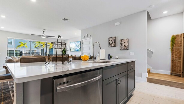 A modern kitchen with a large island, stainless steel appliances, and a view of the living area. - The Serenity Townhome (Kissimmee)