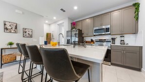 A modern kitchen with a central island, bar stools, stainless steel appliances, and a hanging plant. - The Serenity Townhome (Kissimmee)