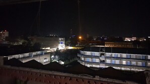 Vista nocturna de un edificio de varios pisos y una torre central, rodeado de otras construcciones.
