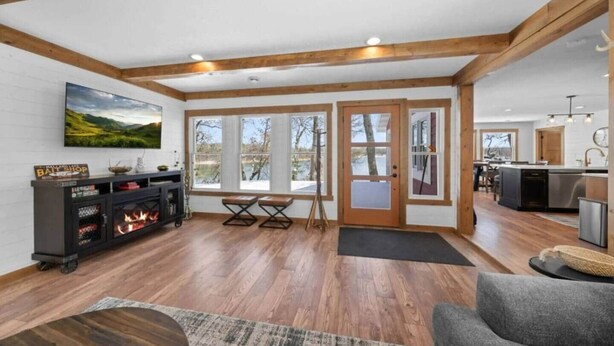 A spacious living area with wooden floors, a fireplace, a dining table, and large windows offering a view of the outdoors. - Mallard Lake Retreat (Jackson)