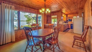 L’intérieur d’un chalet en bois comprend une table à manger, des chaises, un coin cuisine et de grandes fenêtres donnant sur un lac.