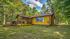 Une cabane en bois jaune, dotée d’une grande porte en verre, entourée d’arbres.