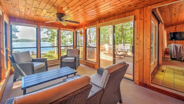Une cabane en bois dotée d’une grande porte-fenêtre coulissante donnant sur une terrasse extérieure, de meubles en osier et d’un ventilateur de plafond.