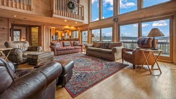 A spacious living room with a large window, a fireplace, and a balcony with a view. - Buckfield Lakehouse | Private waterfront on Rangeley Lake (Rangeley)