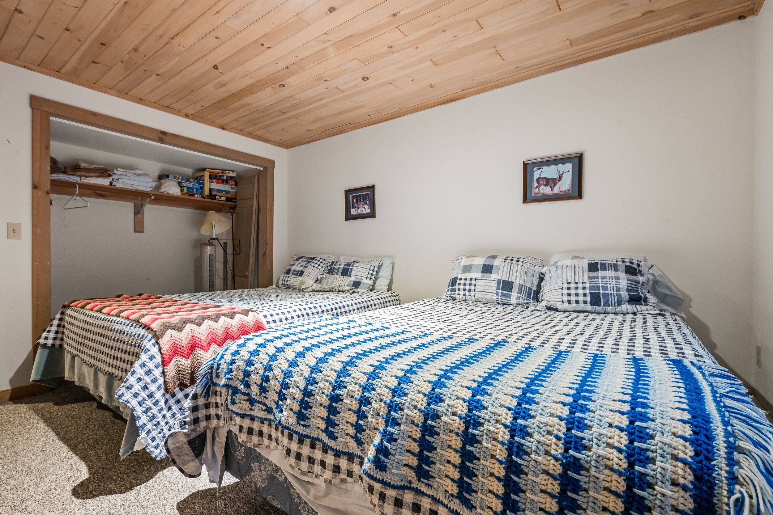 A bedroom with two beds, wooden ceiling, and a closet with shelves.