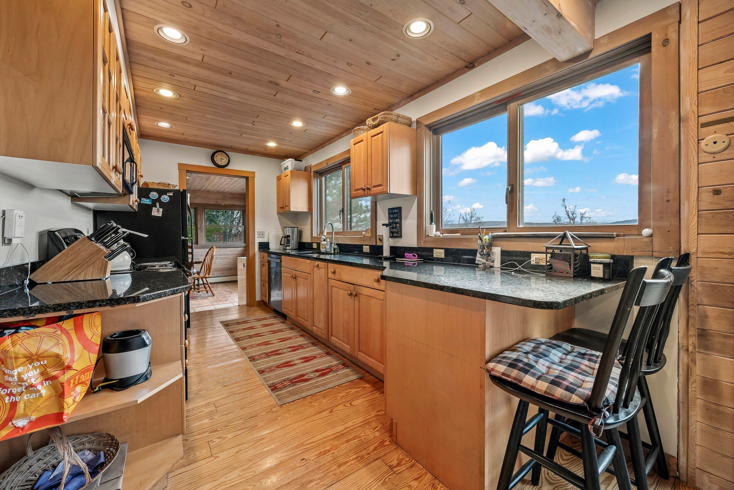 A modern kitchen with wooden cabinets, a black countertop, and a large window offering a view of the sky.