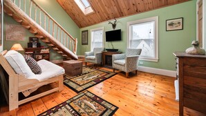 A loft-style room with a wooden staircase, a sofa, armchairs, a flat-screen TV, and a fireplace. - Downtown Crossing Condo | Walk to Town | Pet Friendly | Close to Saddleback (Rangeley)
