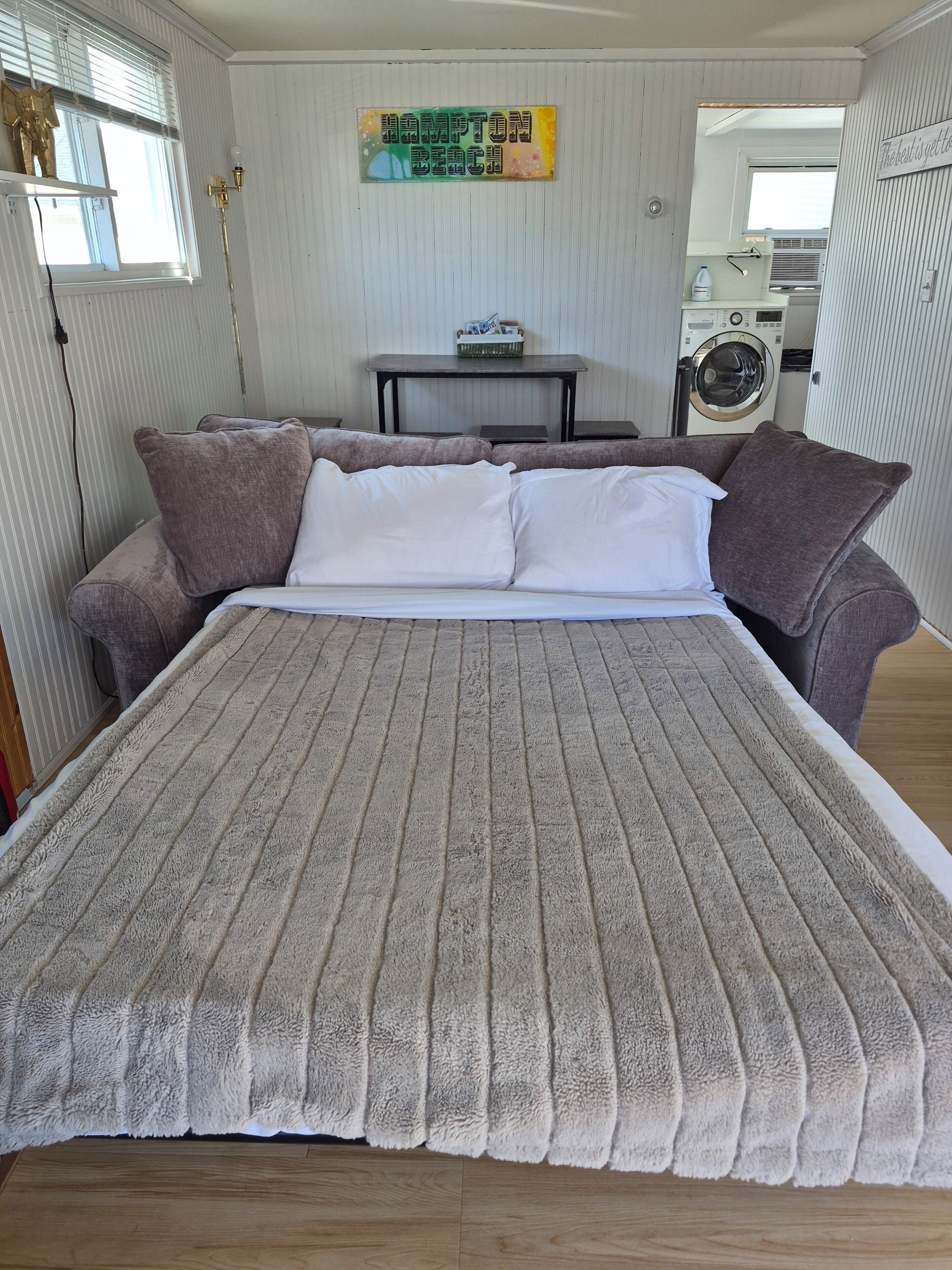 A bedroom with a large bed, two sofas, a table, and a washing machine.