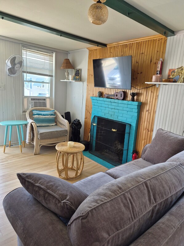 A living room with a fireplace, a sofa, a chair, a television, and a fan.