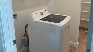 A compact, white front-loading washer and dryer unit in a small laundry room with wooden flooring and white walls. - Lovely studio in charming Hanford perfect for getaway (Hanford)