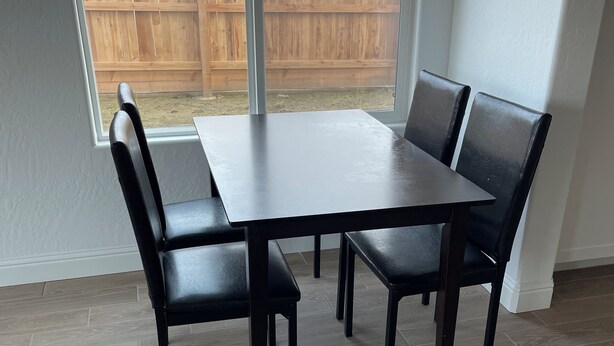 A dining area with a dark wooden table and matching chairs, large windows, and a view of a wooden fence. - Lovely studio in charming Hanford perfect for getaway (Hanford)