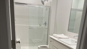 A modern bathroom with a glass shower enclosure, a toilet, and a vanity with a mirror. - Lovely studio in charming Hanford perfect for getaway (Hanford)