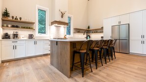 Une cuisine moderne avec des armoires blanches, un îlot central doté de tabourets de bar, un réfrigérateur en acier inoxydable et une tête de cerf accrochée au mur.