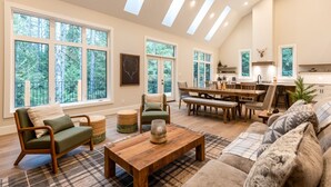 Un salon spacieux avec un haut plafond, de grandes fenêtres, un coin repas et une cuisine.