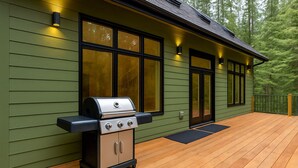 Une maison verte avec une terrasse en bois, un barbecue et de grandes fenêtres.