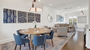 A spacious living room with a large round table, blue upholstered chairs, a sofa, and a ceiling fan. - Live in Luxury at This Brand New Tybee Island Escape | Heated Pool Access (Tybee Island)