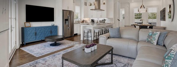 A modern living room with a sofa, coffee table, and bar stools. - Live in Luxury at This Brand New Tybee Island Escape | Heated Pool Access (Tybee Island)