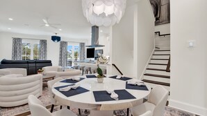 Uma sala de estar moderna com uma mesa de jantar redonda, sofás brancos e uma escada.