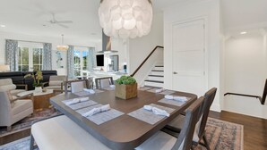 Uma sala de jantar moderna com uma mesa grande, cadeiras, um lustre e uma escada que leva a outro andar.