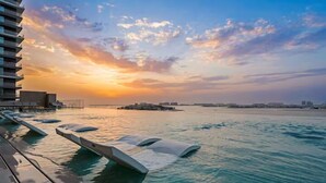 Un espace piscine au bord de l’eau, avec des chaises longues et une vue imprenable sur le coucher de soleil.