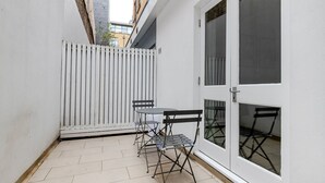 En lille patio med et bord og stole, et hvidt hegn og en dør med glaspaneler.