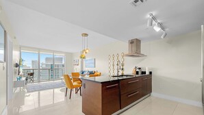 A modern kitchen with a central island, large windows, and a dining area with orange chairs. - Luxury Penthouse with City and Canal View (Miami)