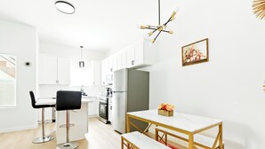 Ett modernt kök med vita skåp, en köksö och en matplats med ett vitt bord och en bänk.