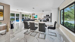 Een moderne keuken met een groot eiland, een eetgedeelte met een glazen tafel en uitzicht op een zwembad.