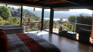 A bedroom with a large bed, a view of the outdoors, a balcony with a table and chairs, and a bathtub. - Acento House (Valle de Bravo)