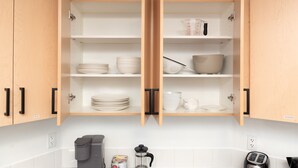 Una cocina con armarios de madera abiertos, estantes blancos y diversos utensilios de cocina.