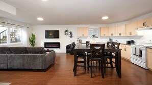 Una sala de estar moderna con un sofá gris, una mesa de comedor con sillas y una zona de cocina con armarios de madera y electrodomésticos.