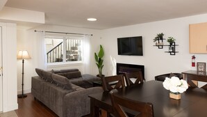 Una sala de estar moderna con un sofá gris, una mesa de comedor de madera y un amplio ventanal con cortinas.