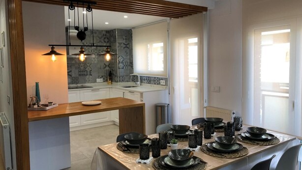 A modern kitchen with a central island, pendant lighting, and a dining area set for a meal. - RIERA Modern Apartment in the Heart of Roses (Roses)