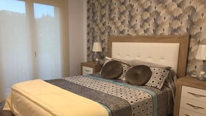 A bedroom with a bed, nightstands, a lamp, and a window with blinds. - RIERA Modern Apartment in the Heart of Roses (Roses)