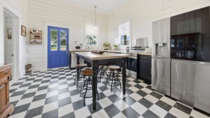 Una cucina con pavimento a scacchi, una porta blu e un'isola centrale con sgabelli.
