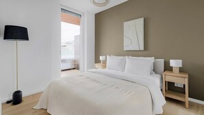 Een moderne slaapkamer met een groot bed, een vloerlamp, een nachtkastje met een lamp, en een stadszicht door een groot raam.