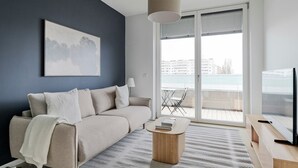 Een moderne woonkamer met een bank, een salontafel, een televisie en een balkon met uitzicht op zee.