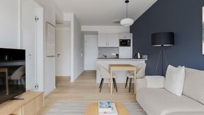 Een moderne woonkamer met een bank, salontafel en een tv-meubel. Er is een keukenhoek met een eettafel en stoelen.