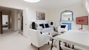 Een moderne woonkamer met een witte zithoek, een eettafel en een open haard. Op de muur hangt een bordje met de tekst 