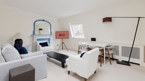 Een moderne woonkamer met een bank, een salontafel, een open haard, een eettafel met stoelen en een staande lamp.