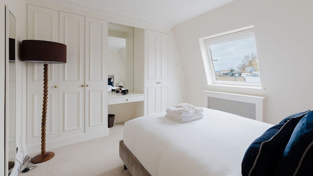 Een slaapkamer met een bed, een kaptafel, een spiegel, een lamp en een raam met uitzicht.