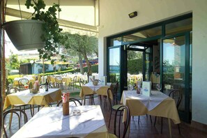 An outdoor dining area with tables set for guests, a hanging planter, and a view of the surrounding garden and buildings. - Mobile home with air conditioning, terrace and pool (Moniga del Garda)
