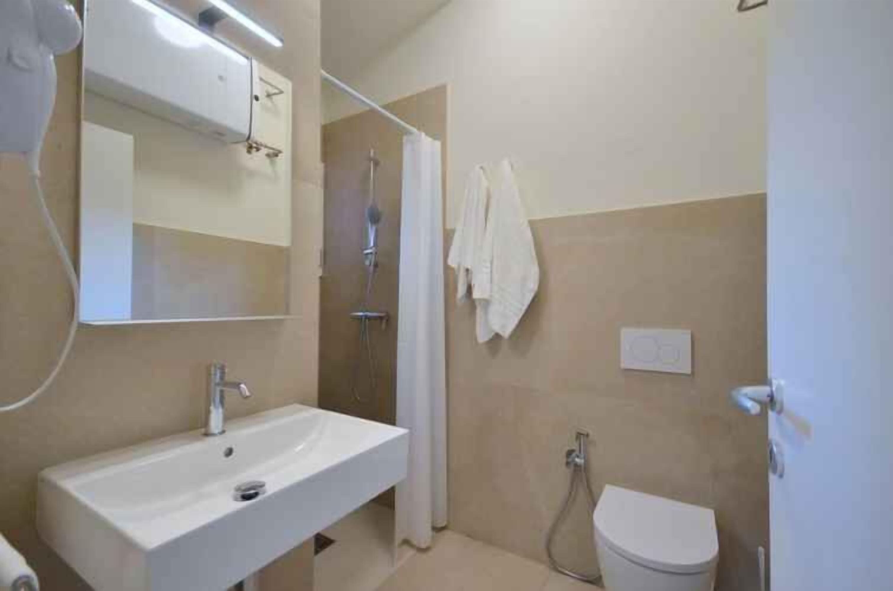 Une salle de bain équipée d’un lavabo, d’un miroir, d’une douche et de toilettes.