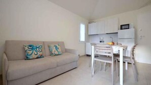 A compact living space with a sofa, dining table, chairs, and a kitchenette with cabinets and a microwave. - Holiday apartment with air conditioning and balcony (Bibione)
