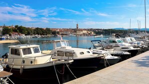Marina com vários barcos atracados, céu claro e vista distante de uma cidade com uma torre imponente.