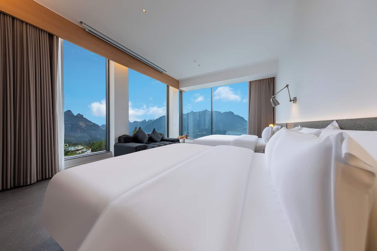 Une chambre d’hôtel moderne avec deux grands lits, un canapé et une vue sur les montagnes.