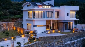 Una casa moderna de dos pisos con un balcón grande y vistas a altas montañas al fondo.