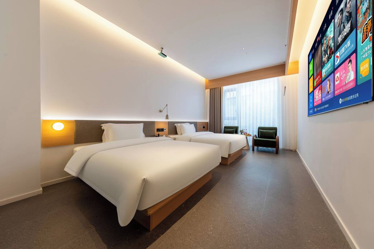 Une chambre d’hôtel avec deux lits, un bureau, une chaise, un mur dédié à la télévision et une grande fenêtre.