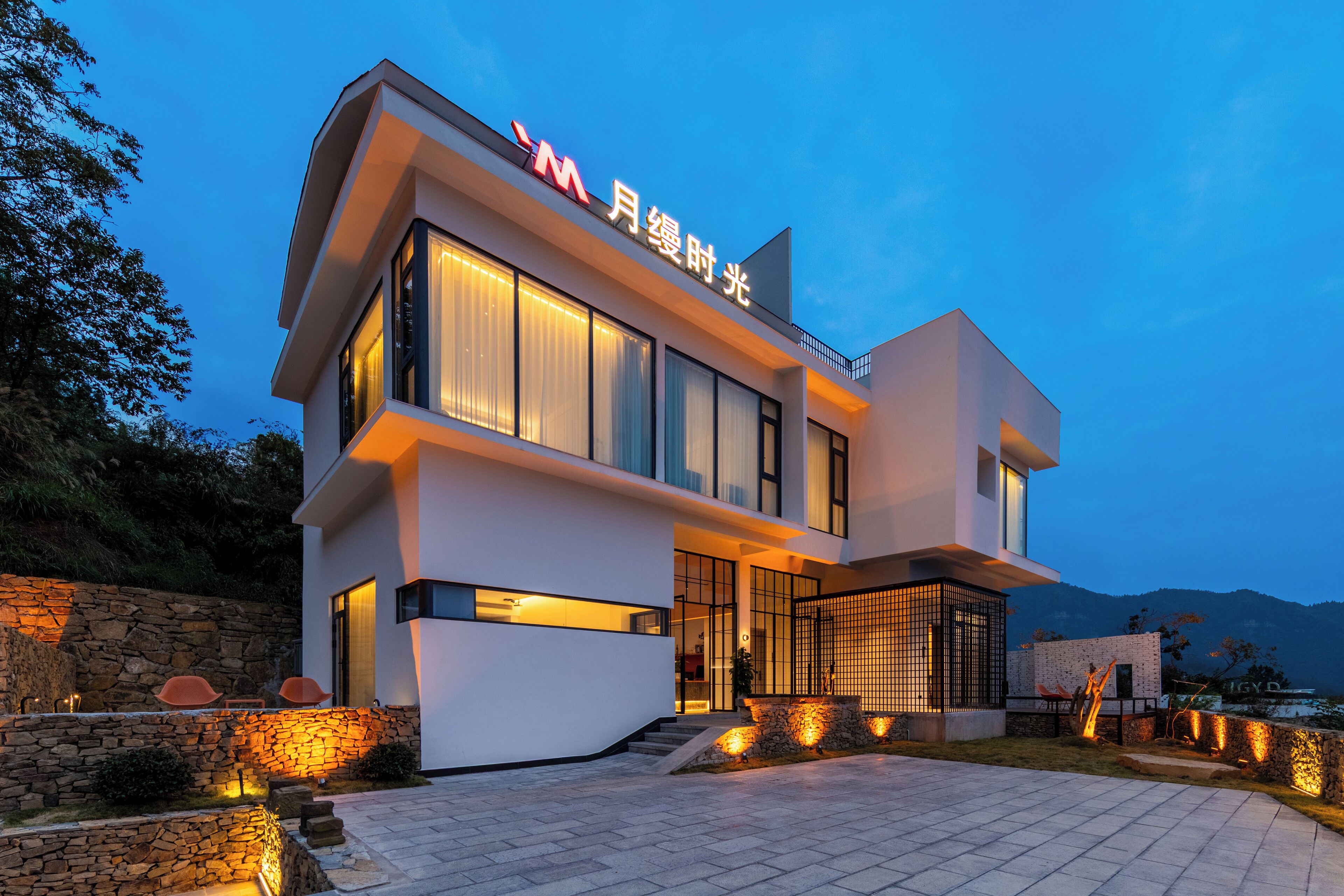 A modern two-story building with a prominent sign, large windows, and a stone wall.