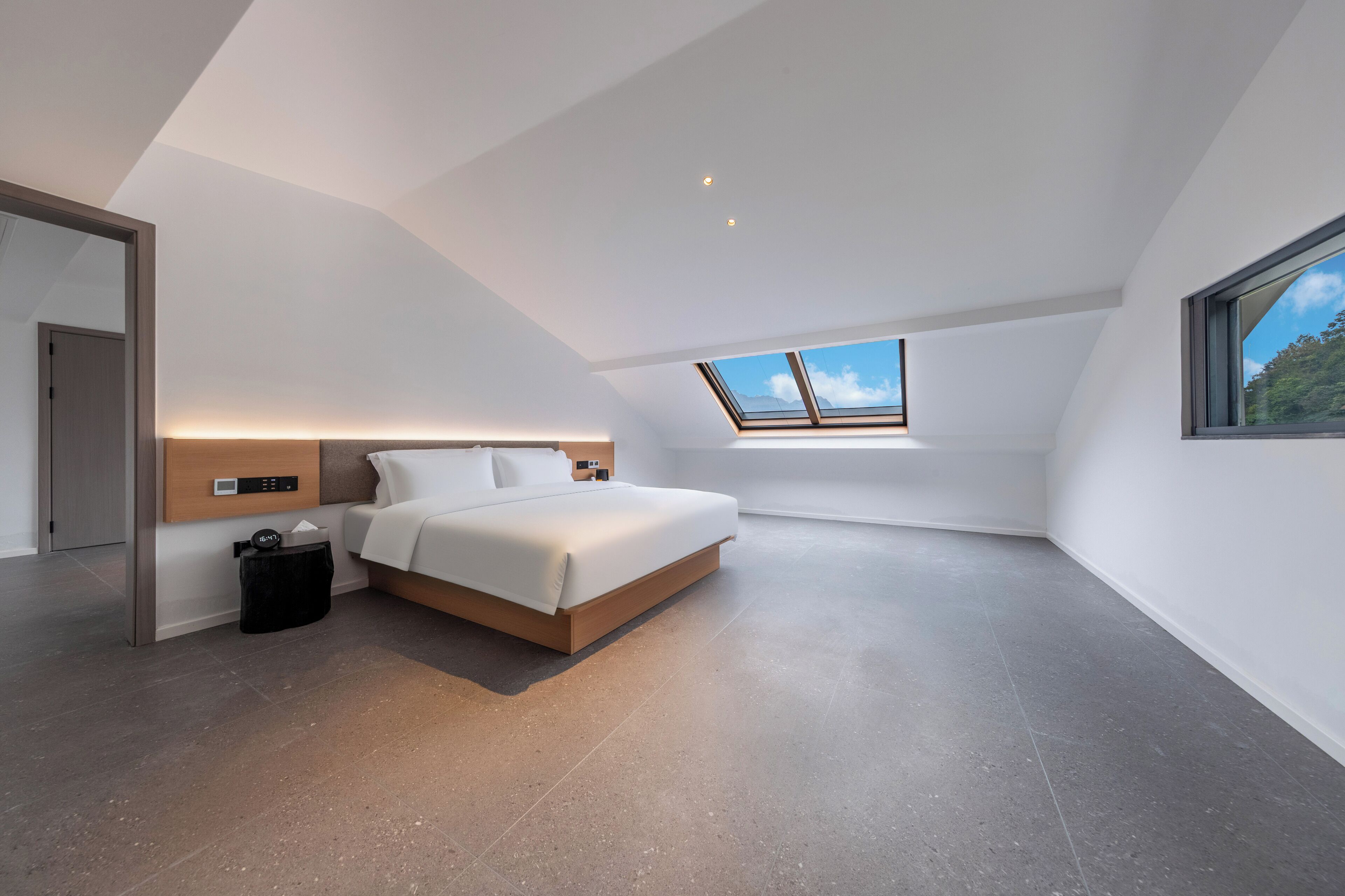 Ein modernes Schlafzimmer mit einem Dachfenster, einem Bett, einem Nachttisch und einer Mülltonne.